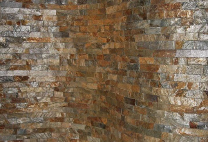 Narożnik ściany z cegły kamiennej w różnych odcieniach brązu, szarości i złota.