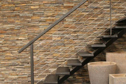 Kamienny mur z czarnymi metalowymi schodami, poręczą kablową i doniczkowymi roślinami.