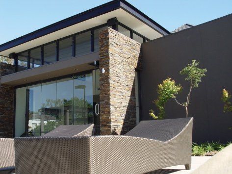 Nowoczesny budynek z kamiennymi akcentami i szklanymi oknami, leżaki na pierwszym planie.