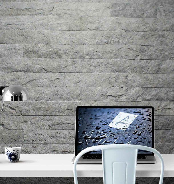 Laptop i krzesło przy białym biurku na tle szarej kamiennej ściany.