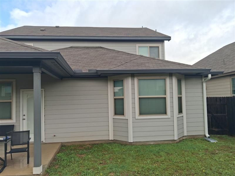 Suburban townhouse exterior with beige siding, green grass, and a covered patio and windows.