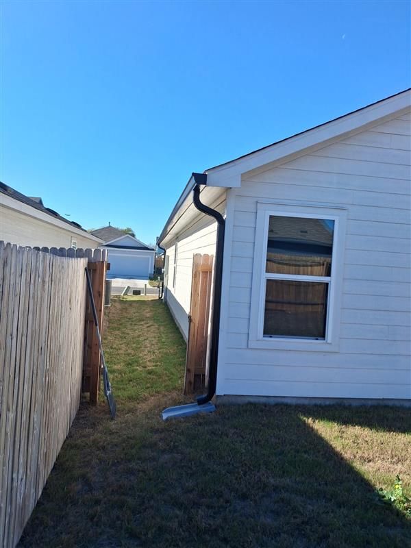 Narrow grass path between two houses, with a white house and wooden fence under a blue sky.