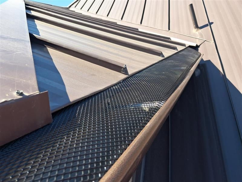 Close-up of a metal roof with a black textured walkway beside light gray standing seams.