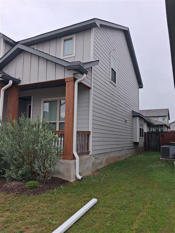 Two-story gray house with covered front porch and green yard on an overcast day