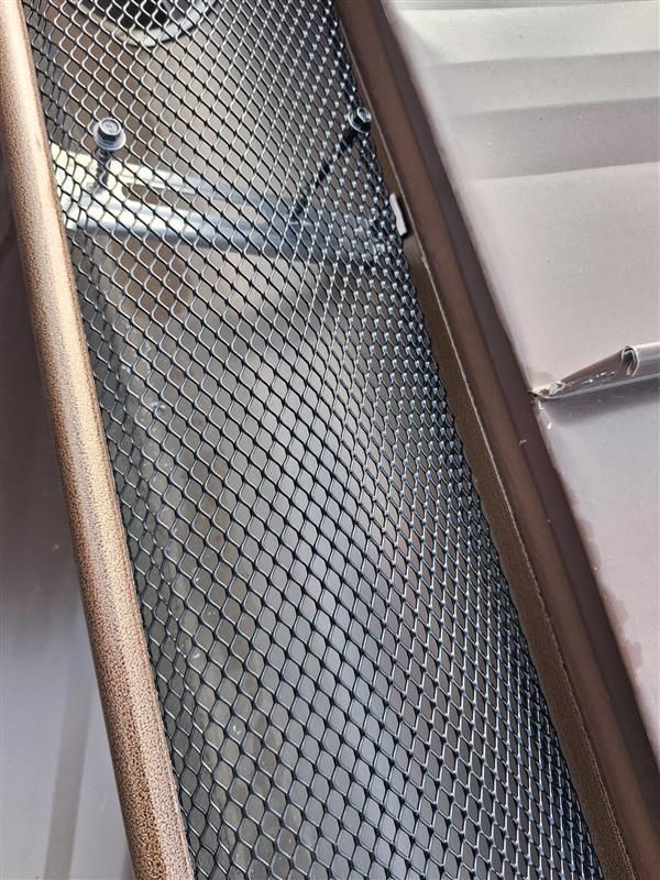 Tilted view of a metal mesh stair railing beside a staircase with white walls and brown trim