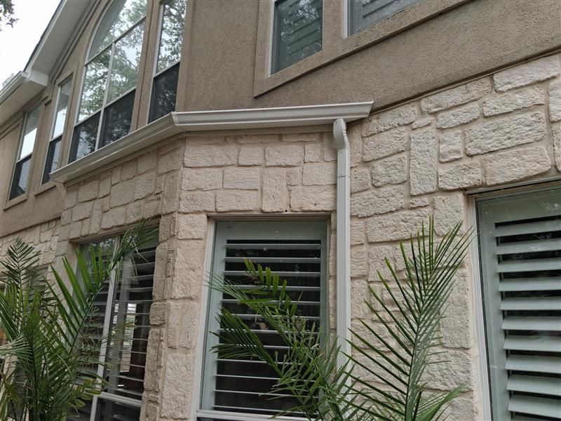 Exterior of a beige stone house with windows and palm plants in front