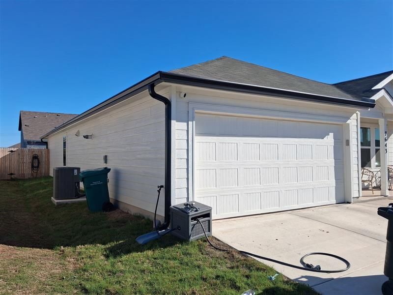 Suburban house exterior with white garage door, driveway, and grass yard on a sunny day