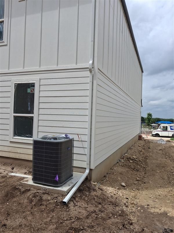 White-sided house exterior with a window, air conditioner, and dirt yard under cloudy sky
