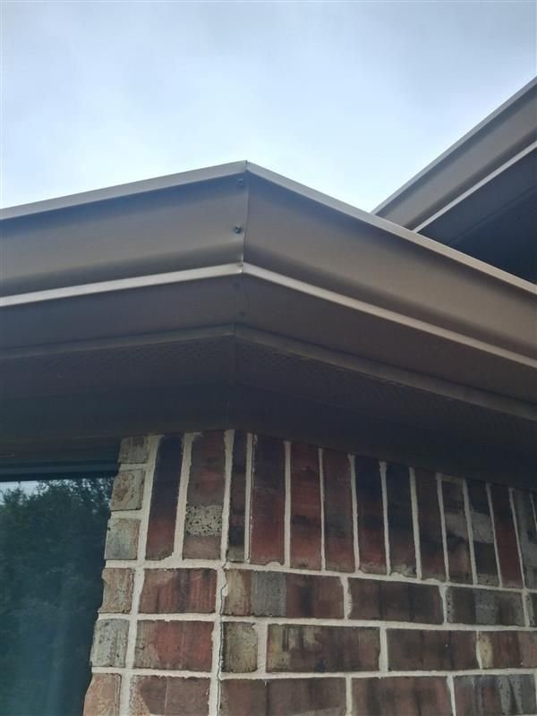Corner of a brick house with a dark roof eave against a cloudy sky