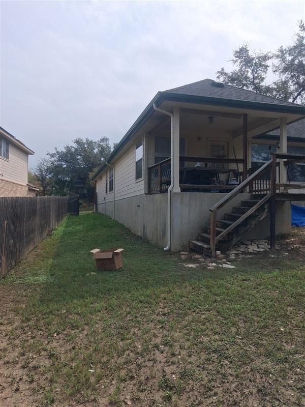 Narrow grassy side yard between houses with a small porch and stairs on the right, overcast sky above
