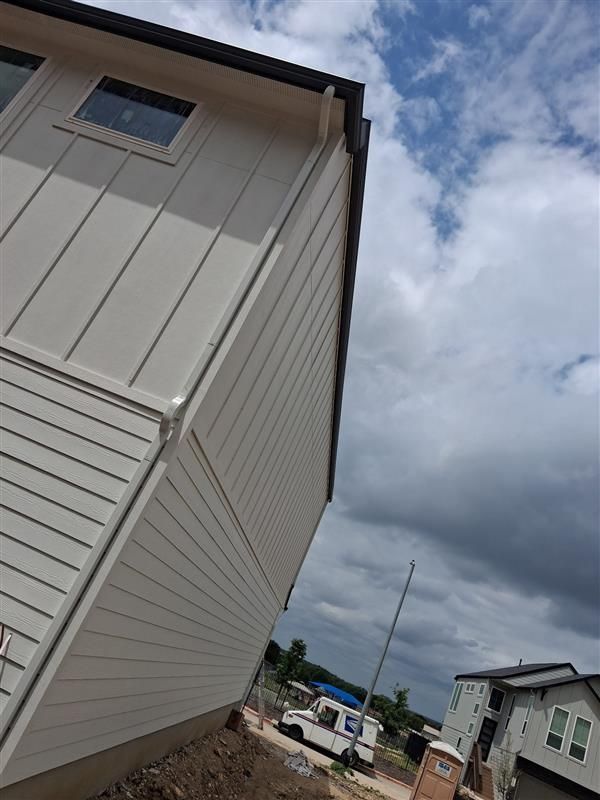 Tilted view of a beige house beside a dirt road under a cloudy sky