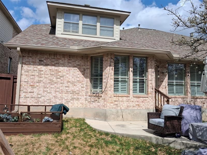 Backyard patio with brick house, windows, and outdoor furniture covered in protective tarps