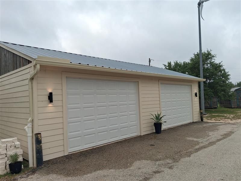 Two-car beige garage with white doors and a small potted plant outside