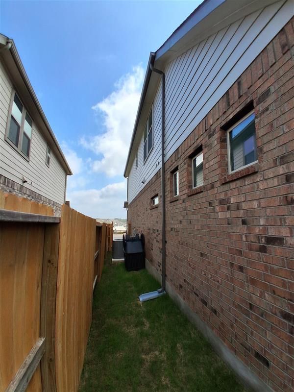 Narrow grassy side yard between brick and wood houses with a fence and blue sky.