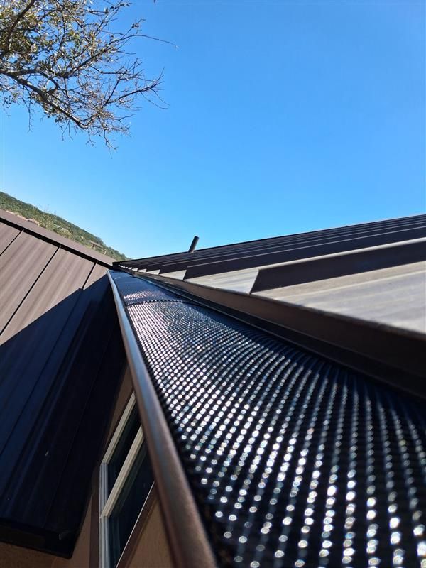 Black metal roof valley with skylight under blue sky and tree branches