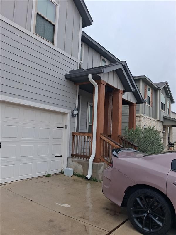 Residential townhouse driveway with garage, covered porch, and a pink car parked in front.