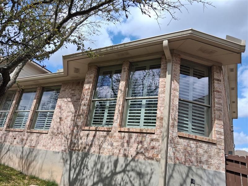 Brick house exterior with white shutters and a tree casting shadows across the wall