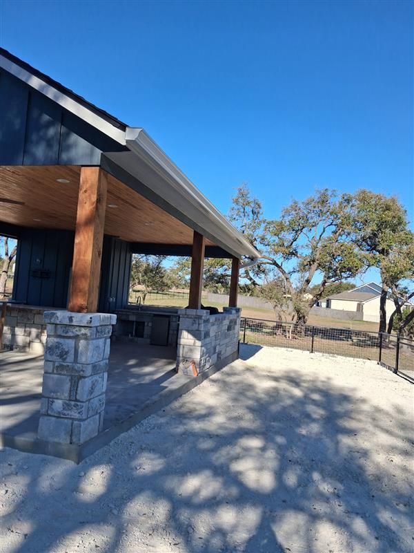 Stone porch of a modern building with a wooden roof, casting long shadows on a sunny day.