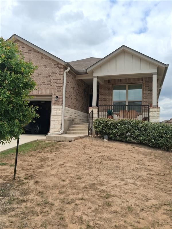 Suburban brick house with front porch, steps, and a dry lawn under cloudy skies