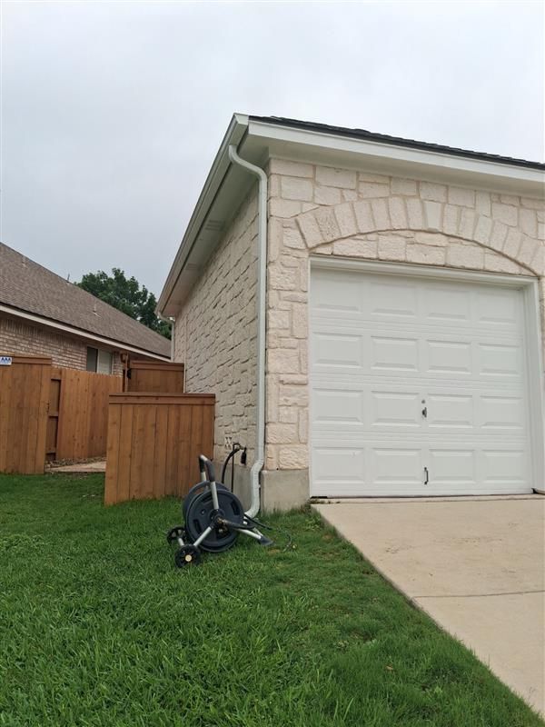 House exterior with stone garage, white door, driveway, lawn, and a bicycle near the fence