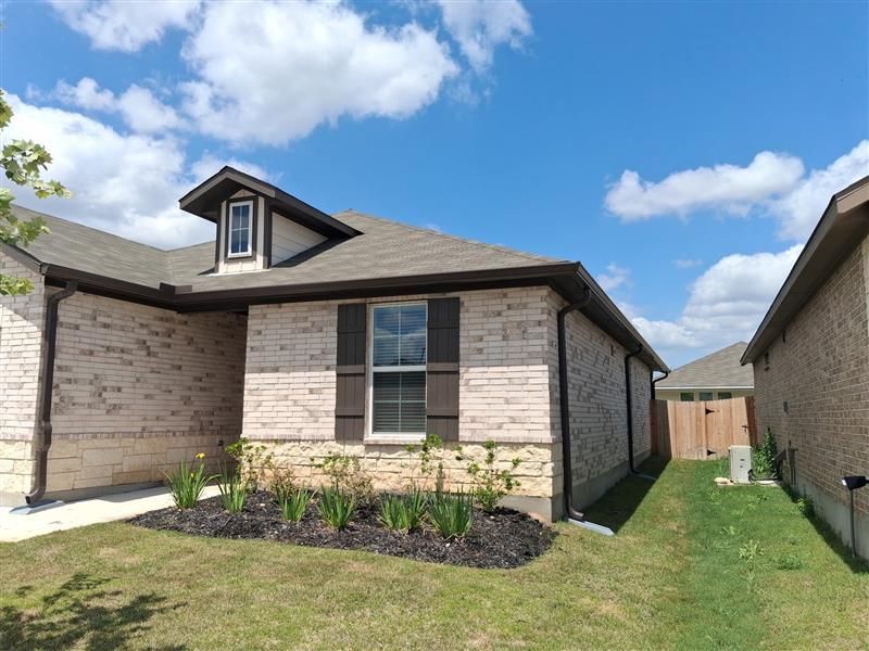 Single-story brick house exterior with a small dormer, grass yard, and blue sky with clouds