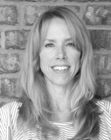 A woman is smiling in front of a brick wall in a black and white photo.