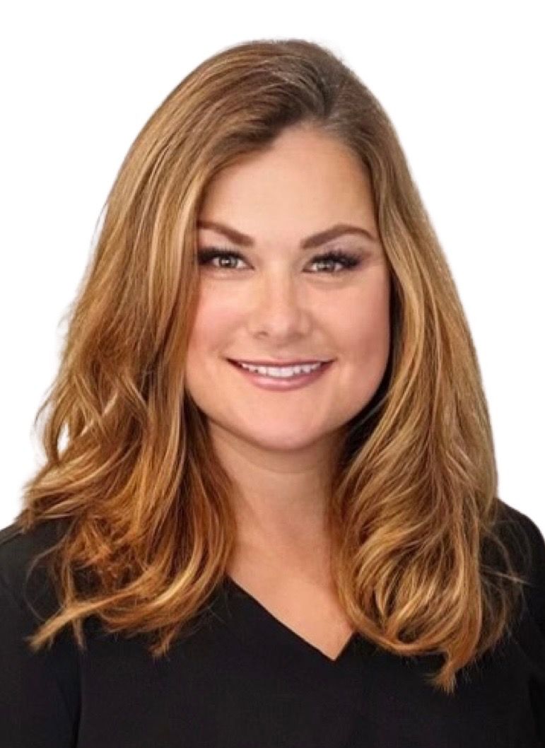 Woman with long wavy brown hair smiling, wearing a black shirt, and posing against a white backdrop.