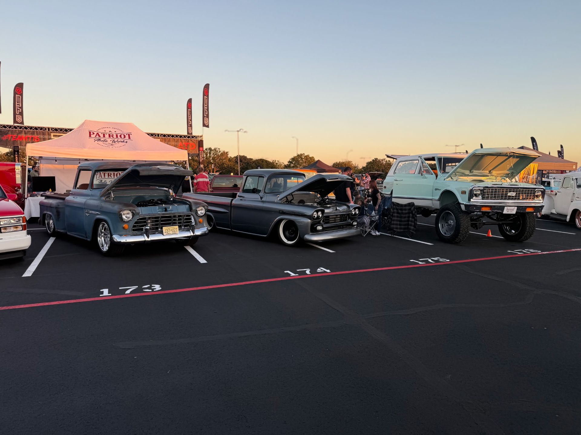 Classic trucks parked at an outdoor car show; light blue, dark blue, and gray vehicles with hoods open.