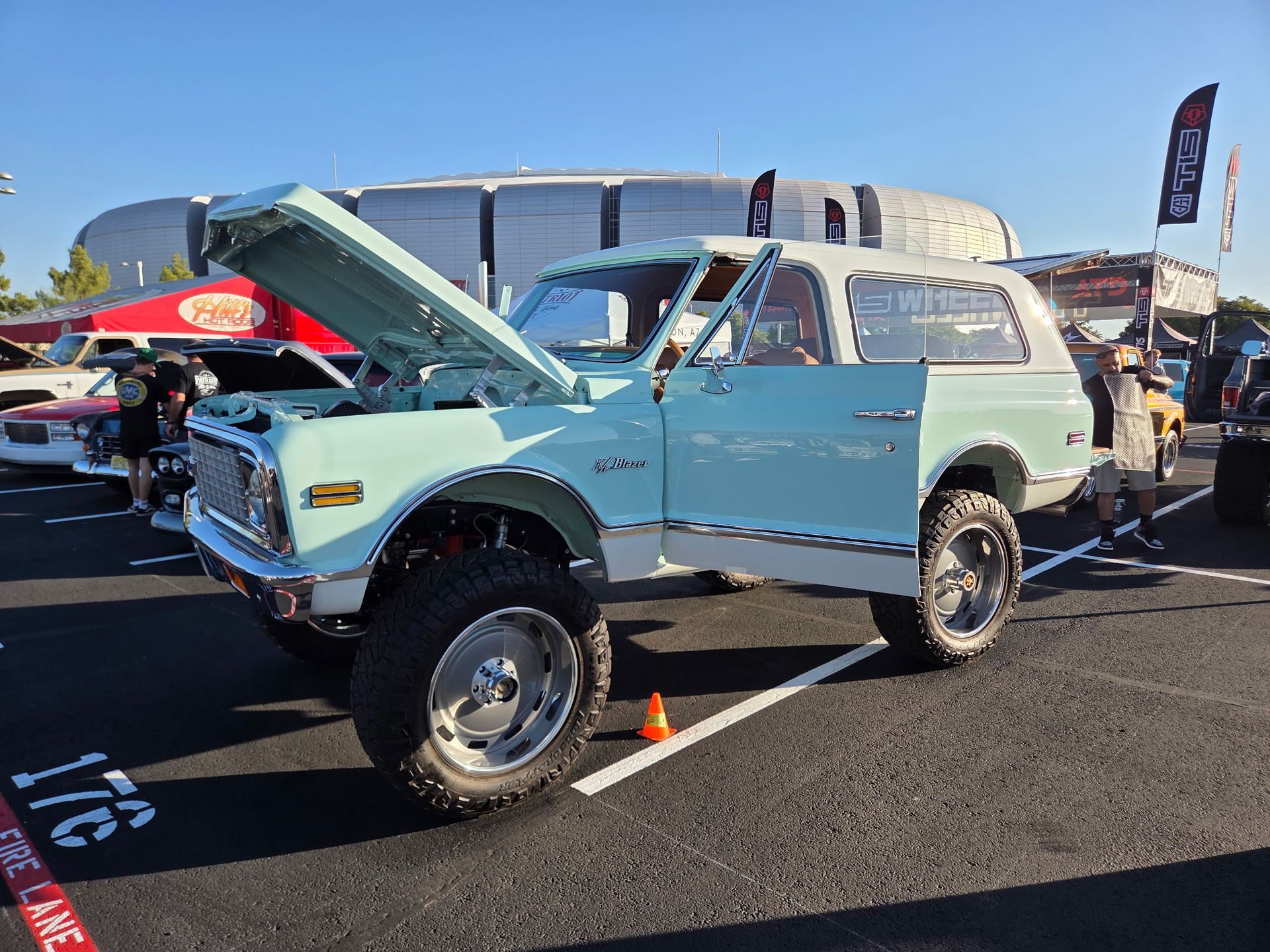 Light blue and white lifted Chevy Blazer with open hood and door at a car show.