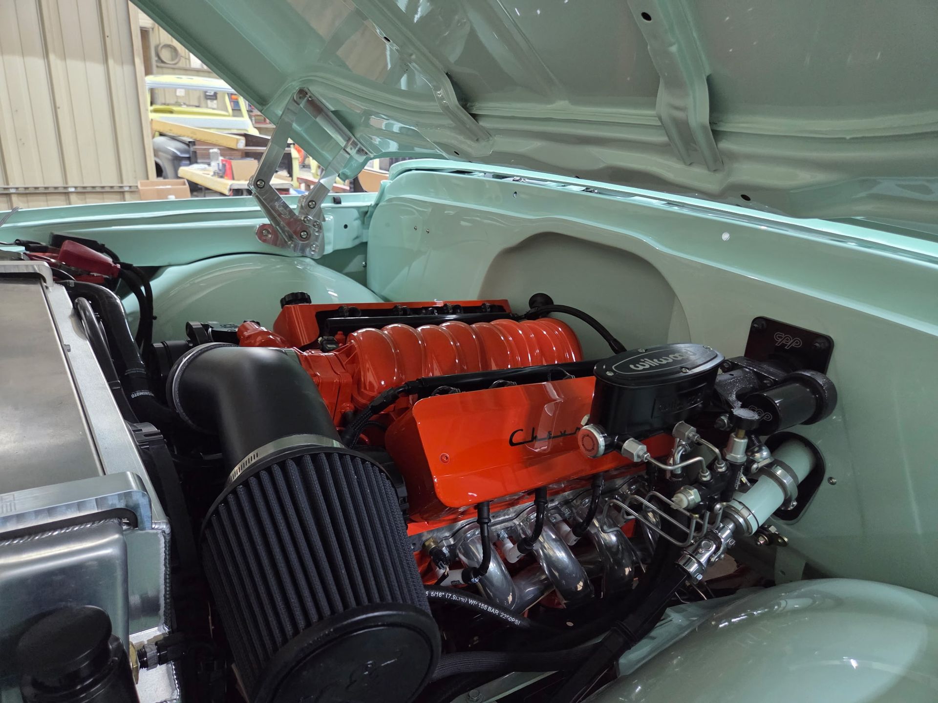 Engine bay of a classic vehicle with an orange engine and black air filter, painted in a light blue hue.