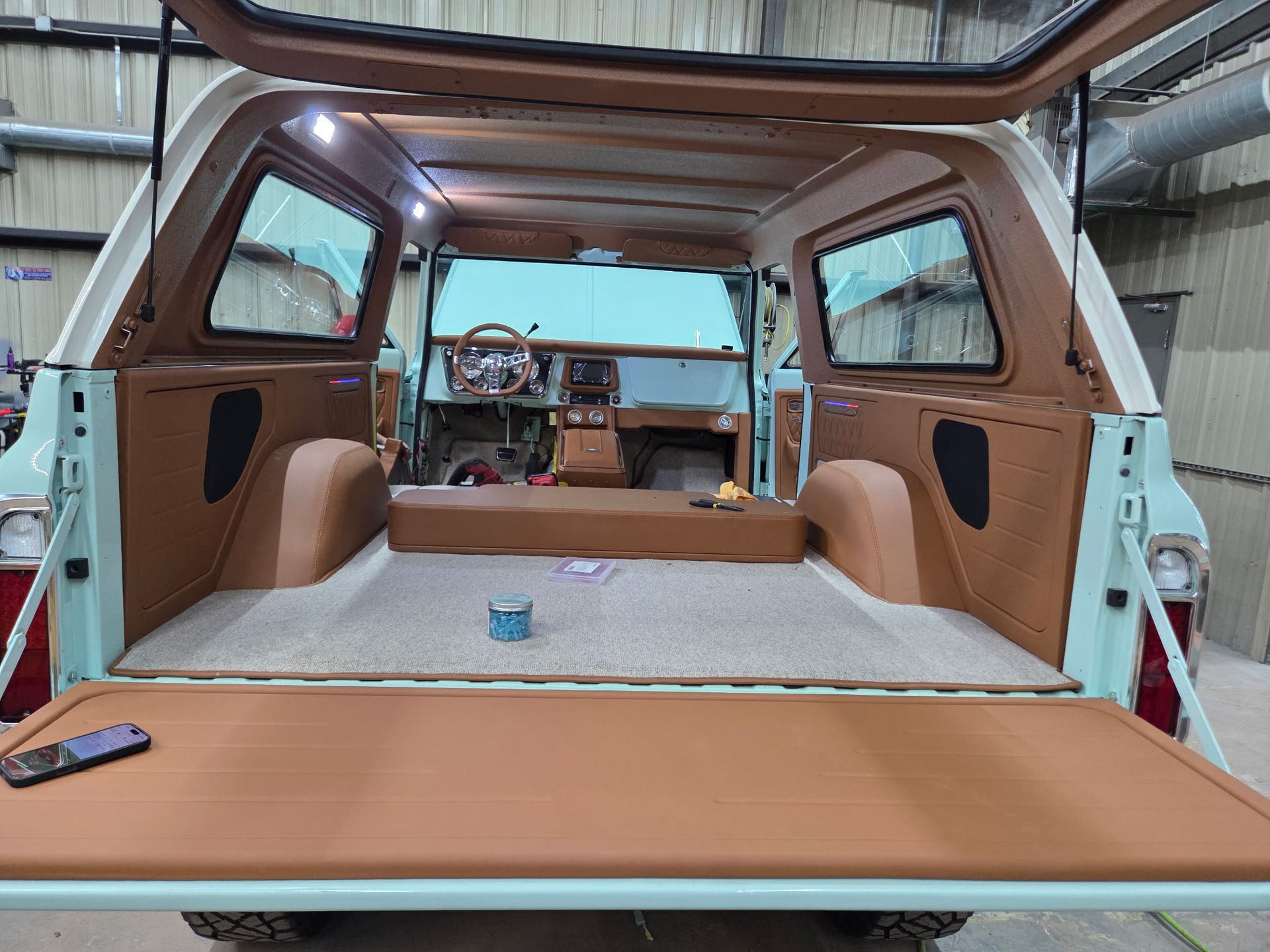 Interior of a classic SUV with brown and beige upholstery, open tailgate, and carpeted floor.