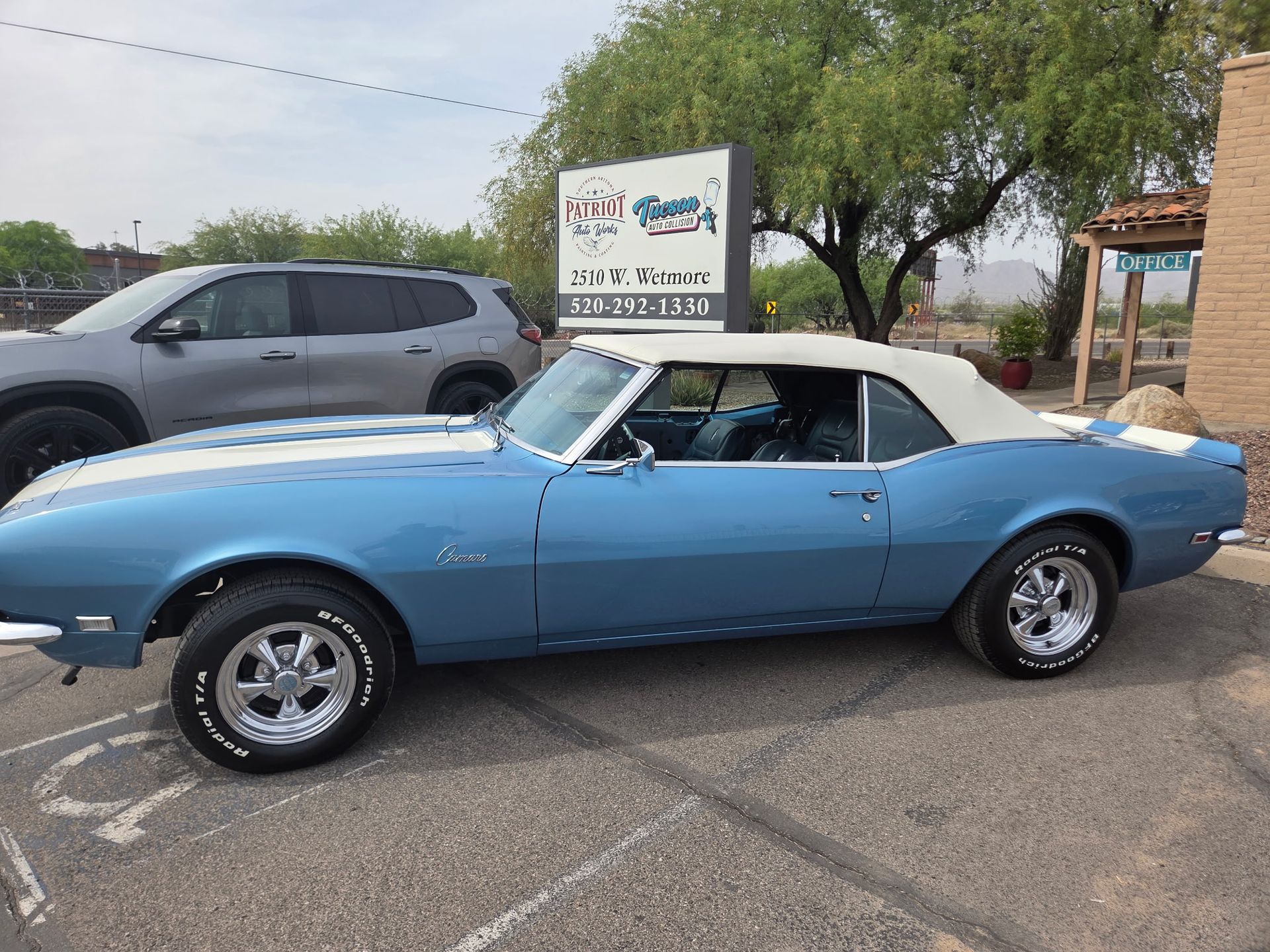 Blue classic convertible parked in a lot beside a gray SUV and a roadside sign