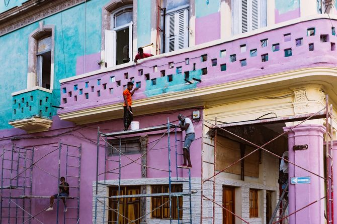 A paint roller and two paintbrushes covered in terracotta-colored paint, resting against a painted wall of the same color.