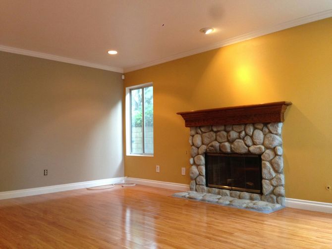 A worker suspended by ropes paints a white stripe on the exterior wall of a tall, light-brown building.