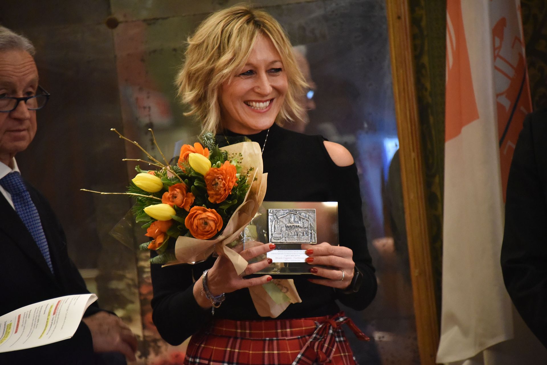 Una donna tiene in mano un mazzo di fiori e un certificato.