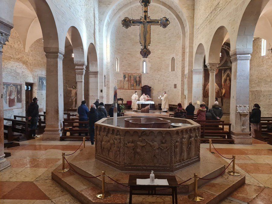 L'interno di una chiesa con fonte battesimale e una croce appesa al soffitto.