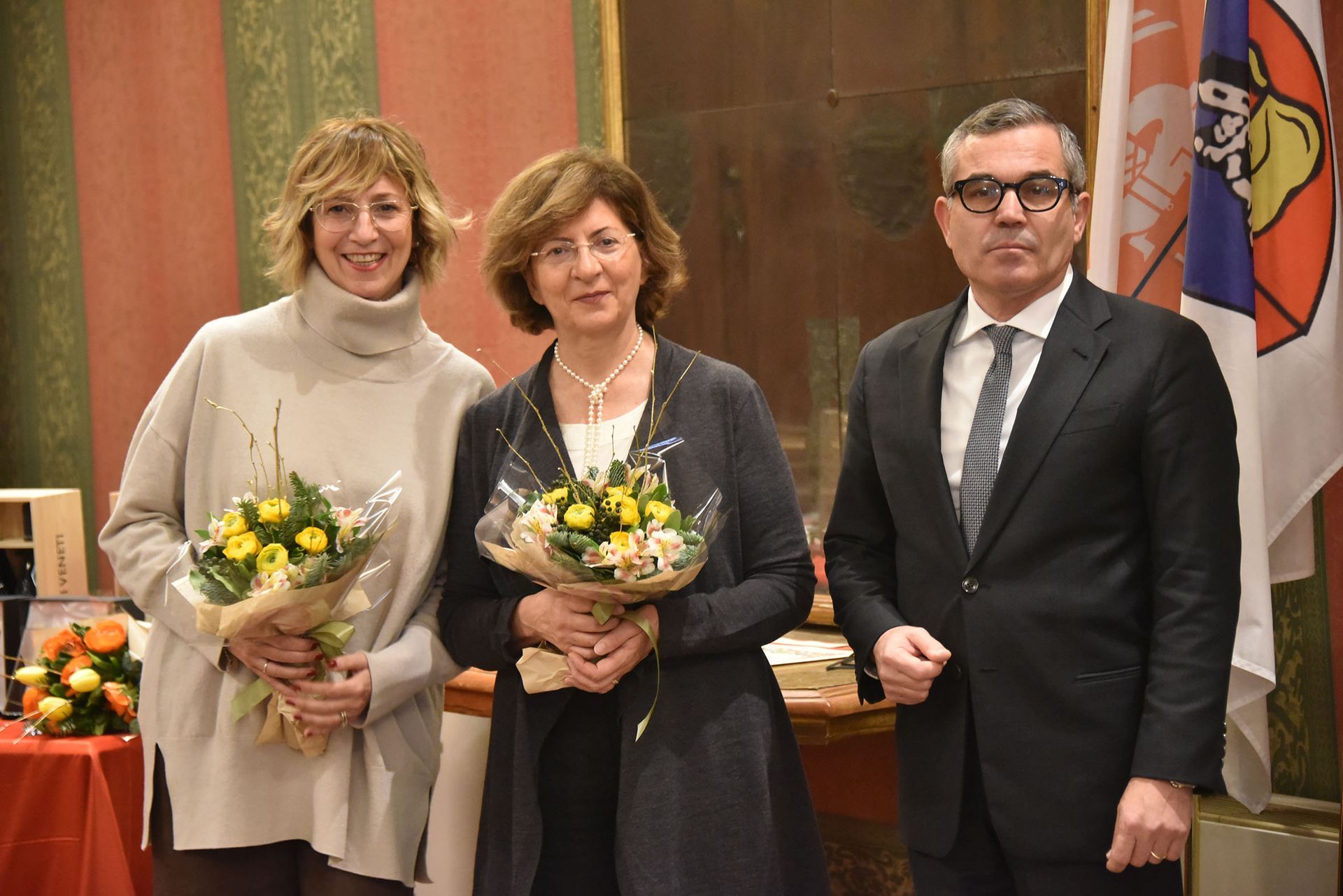 Tre persone sono in piedi una accanto all'altra con in mano mazzi di fiori.