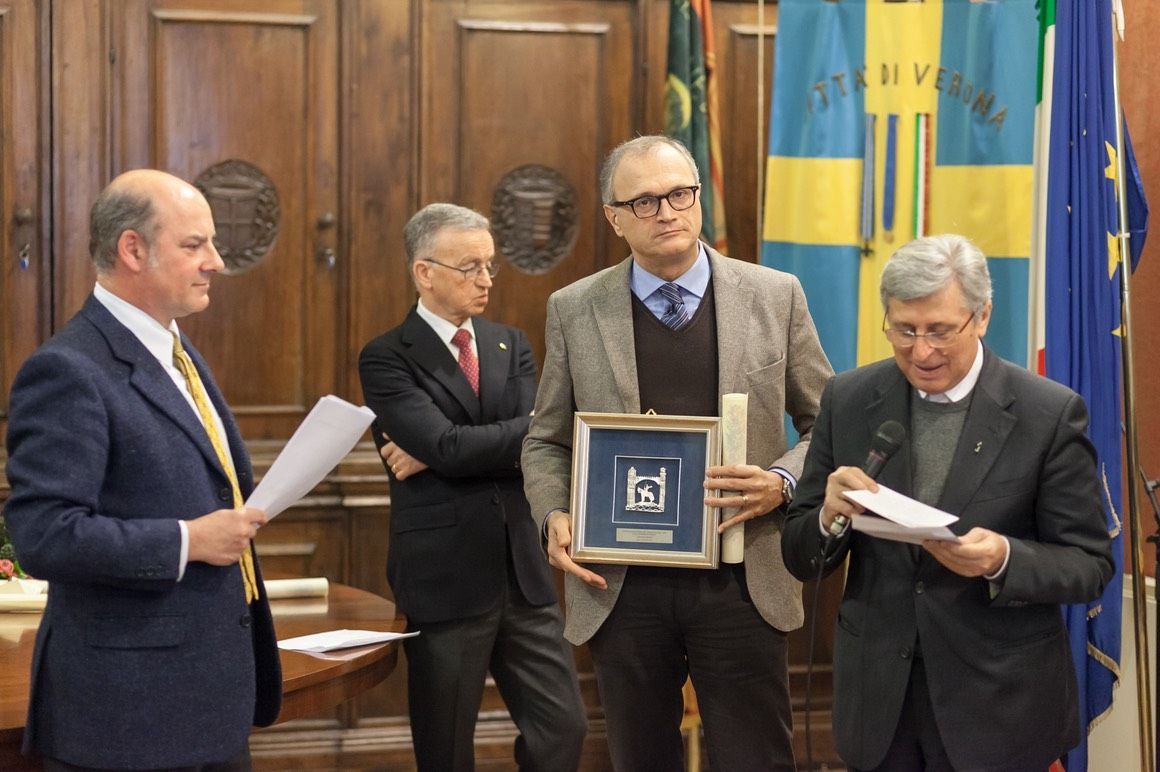 Un gruppo di uomini in giacca e cravatta è in piedi in una stanza con le bandiere sullo sfondo.