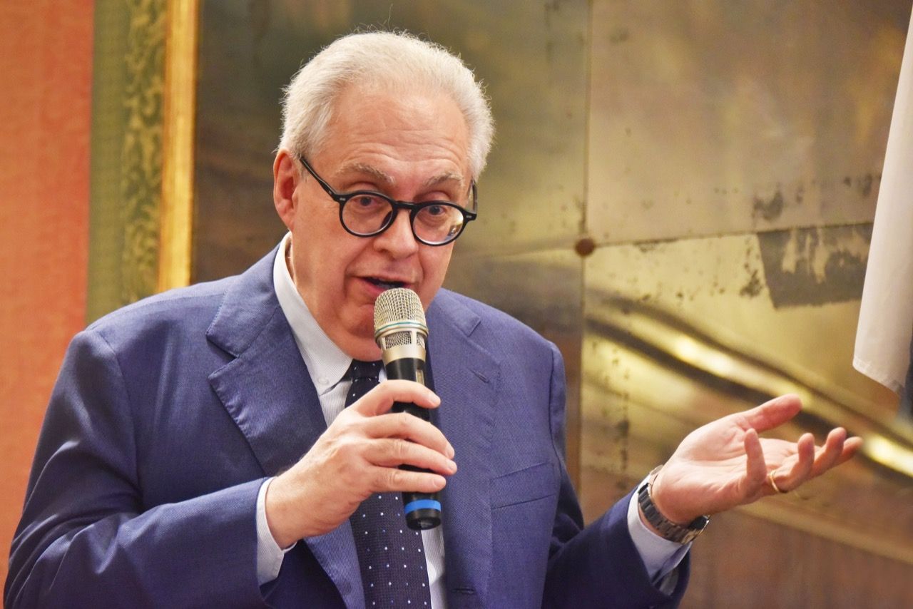 Un uomo in giacca e cravatta parla al microfono.