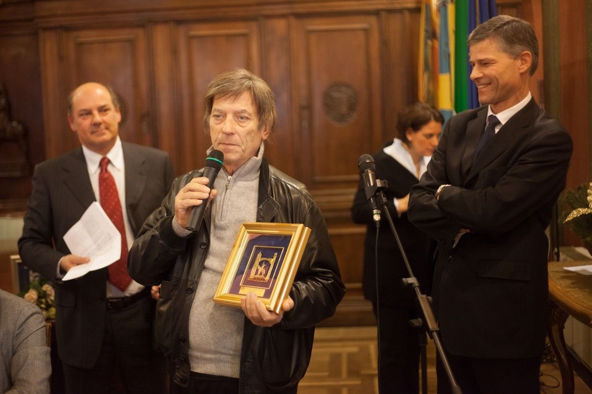 Un uomo tiene in mano un'immagine incorniciata mentre parla al microfono.