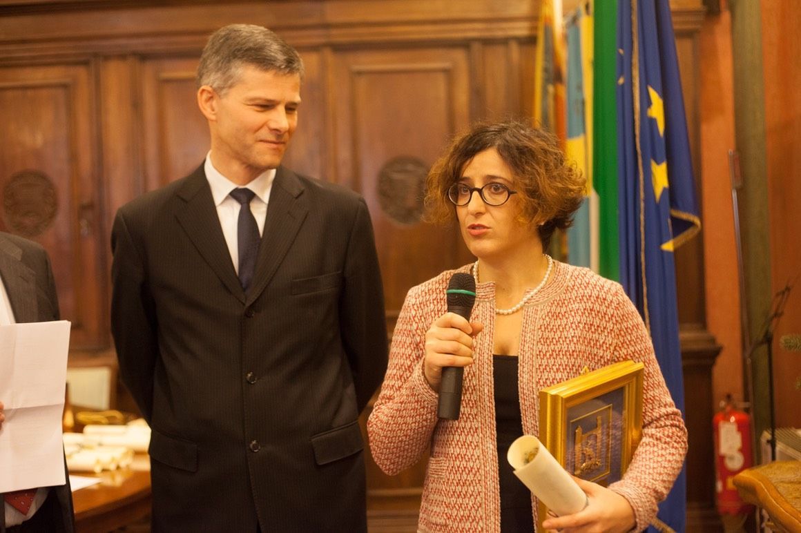 Una donna tiene in mano un microfono mentre è in piedi accanto a un uomo in giacca e cravatta.