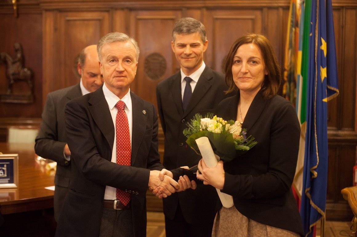 Una donna tiene in mano un mazzo di fiori e stringe la mano a un uomo in giacca e cravatta.