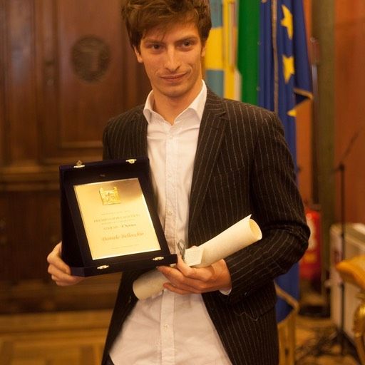 Un uomo in giacca e cravatta tiene in mano una targa e un diploma