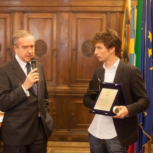 Un uomo in giacca e cravatta tiene in mano un microfono mentre un altro uomo tiene in mano una targa