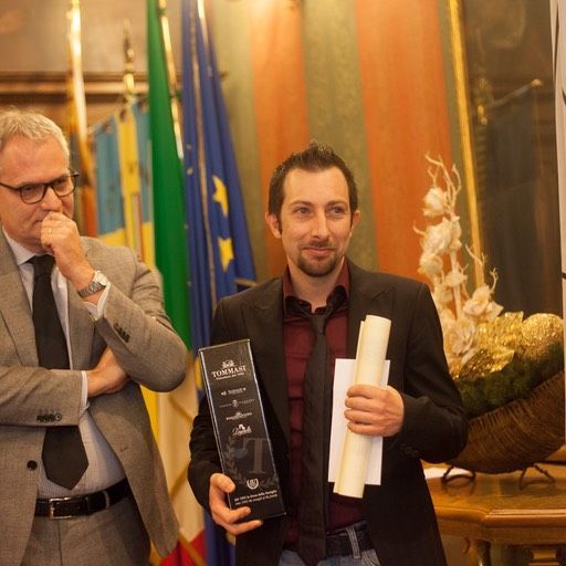 Un uomo in giacca e cravatta tiene in mano un premio