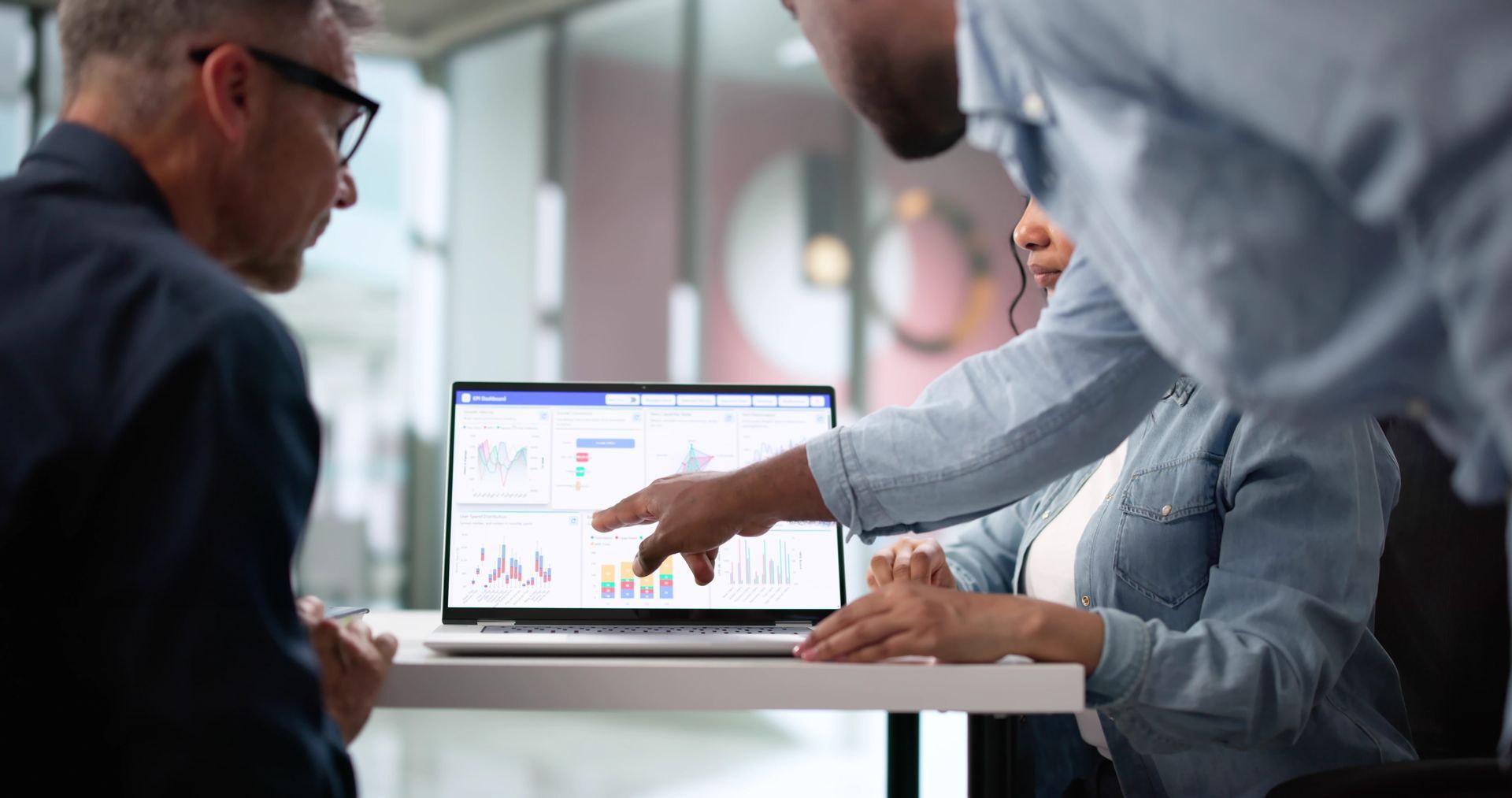 Three people reviewing data on a laptop screen in a modern office.