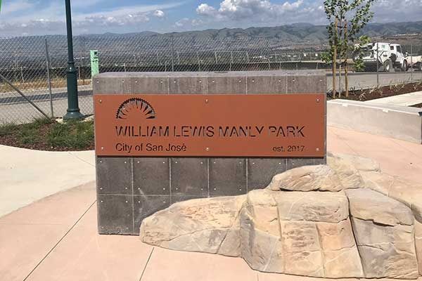 Sign for William Lewis Manly Park in San Jose. Brown and gray sign with text and an emblem of a sunrise.