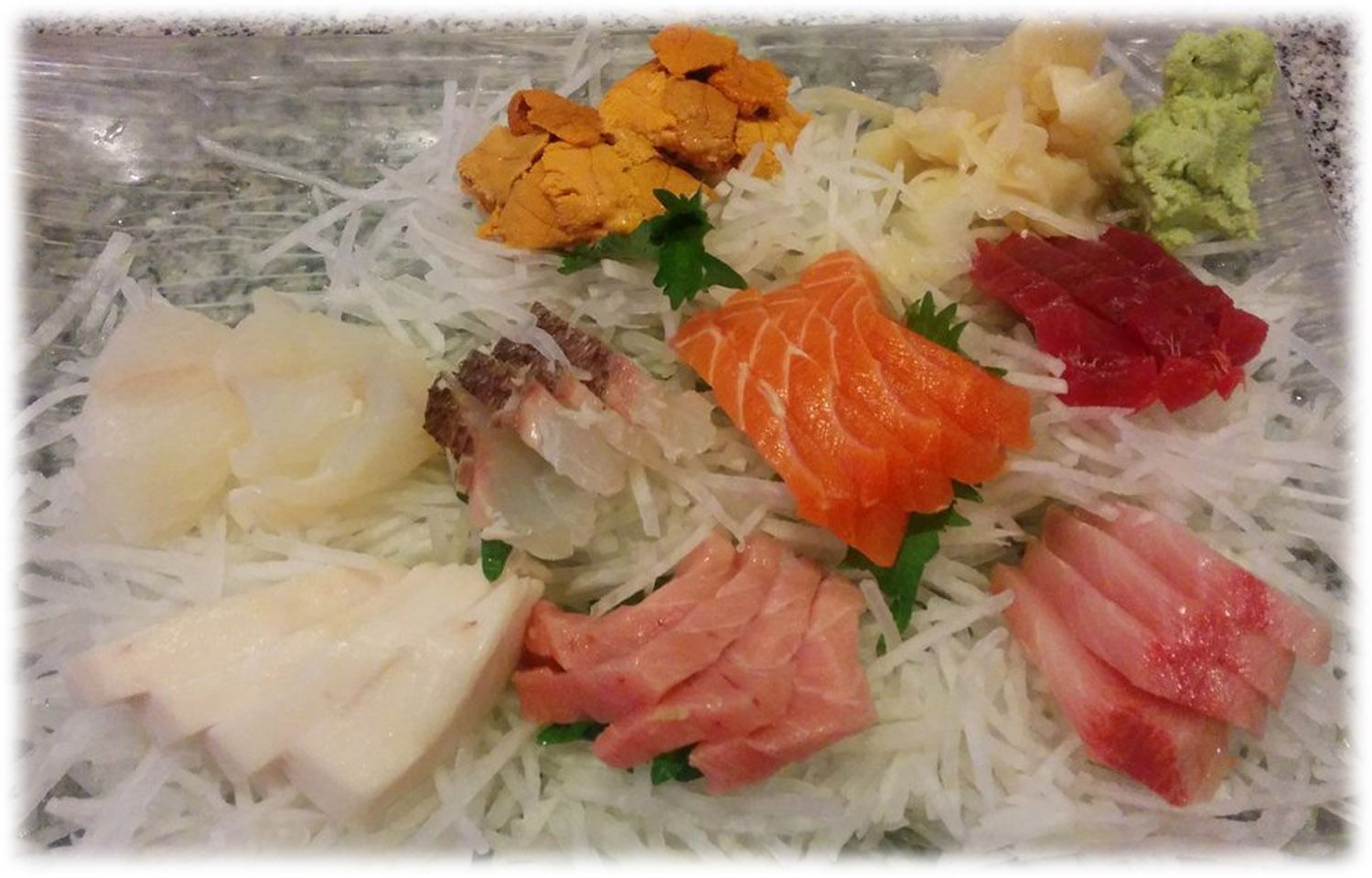 Assorted sashimi platter arranged on shredded daikon radish, including salmon, tuna, and sea urchin.