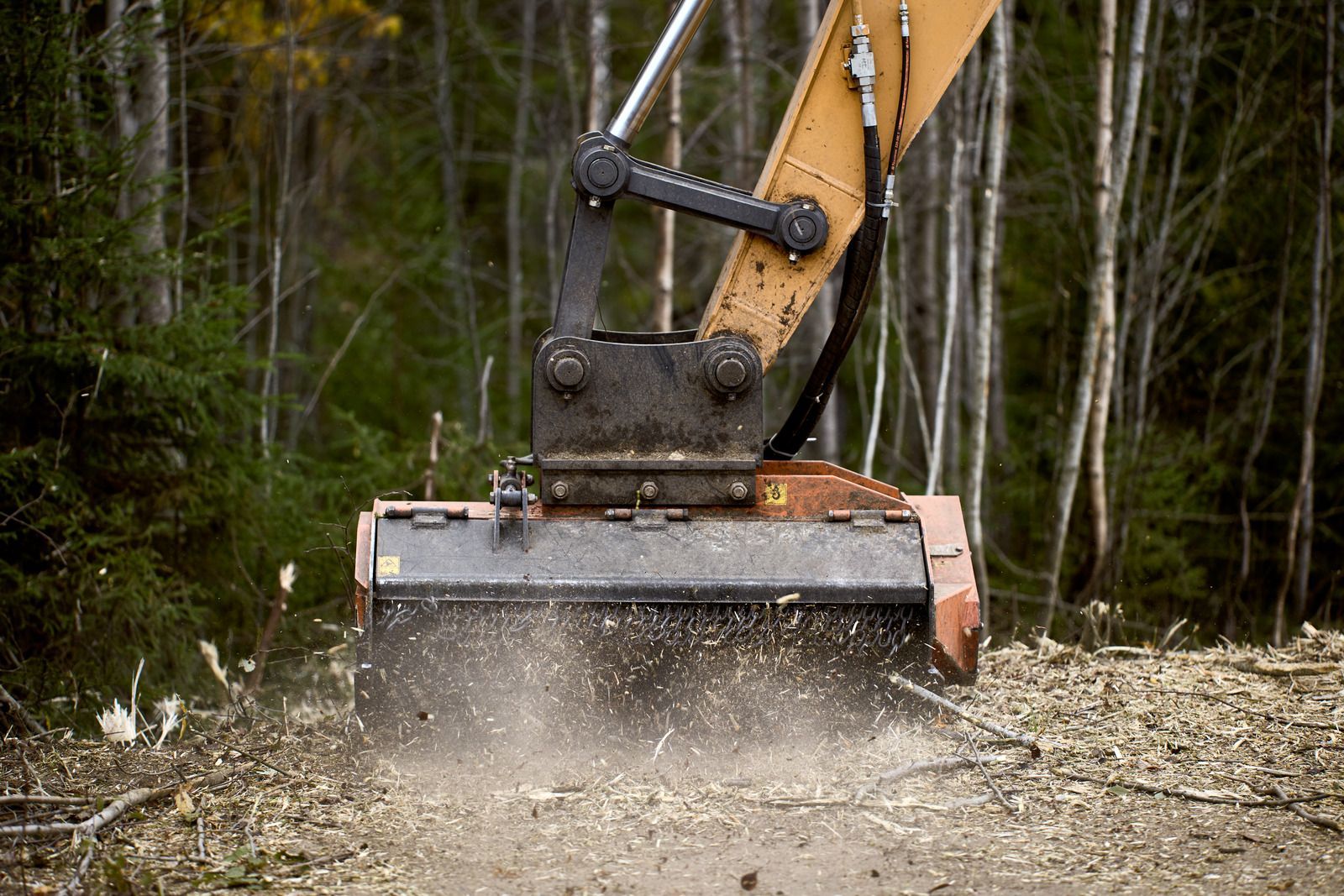 Excavator attachment grinding soil and gravel at a forest construction site