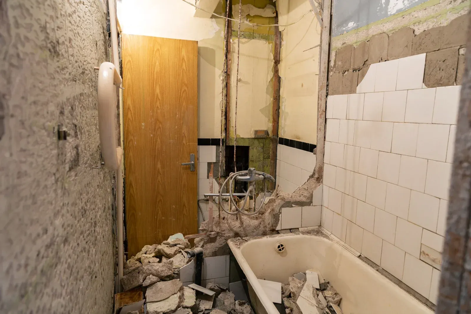 Bathroom with damaged walls, debris on the floor, and a partially destroyed bathtub area
